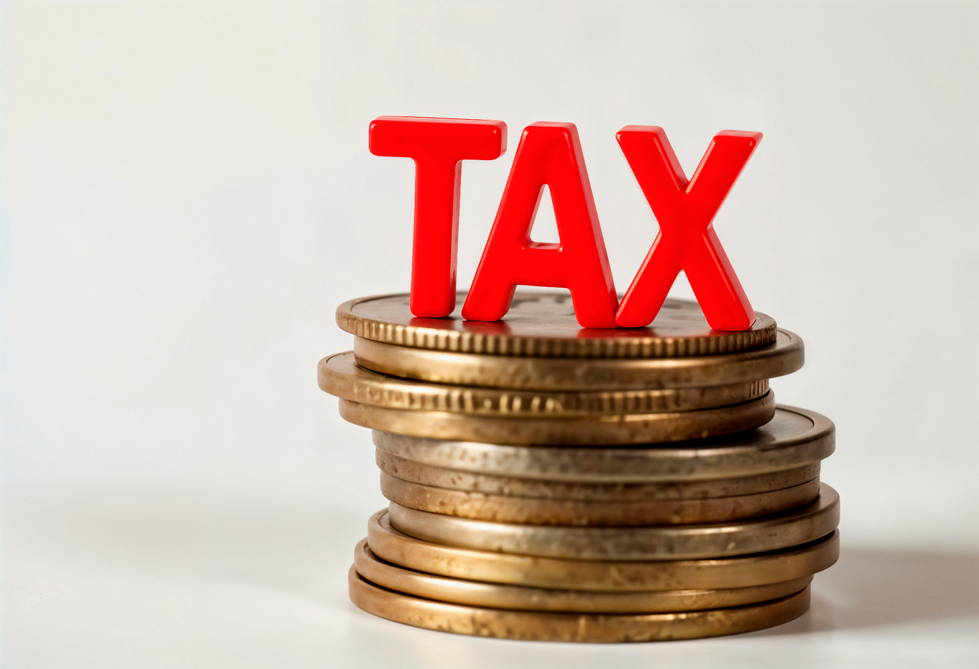 ตัวอักษร TAX สีแดงวางบนกองเหรียญ สื่อถึงภาษีมูลค่าเพิ่ม